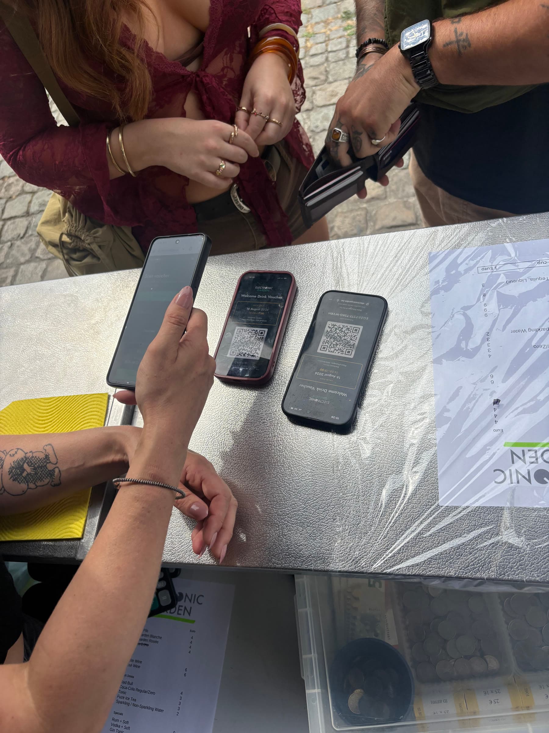 Hands and phones on the welcome desk, drink vouchers open on the screens.