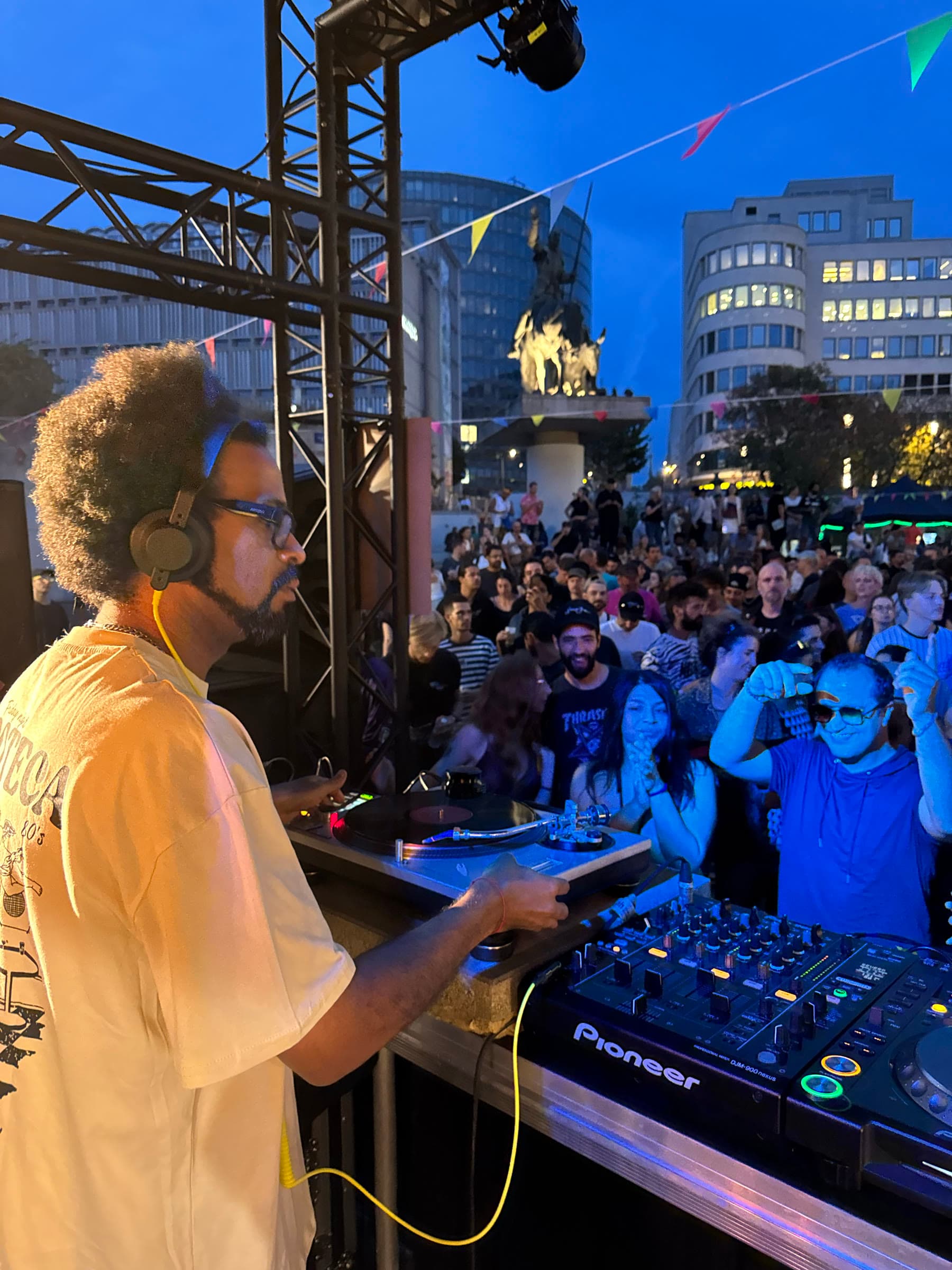 A DJ at the decks as the sky turns deep blue over the crowd and the statue.