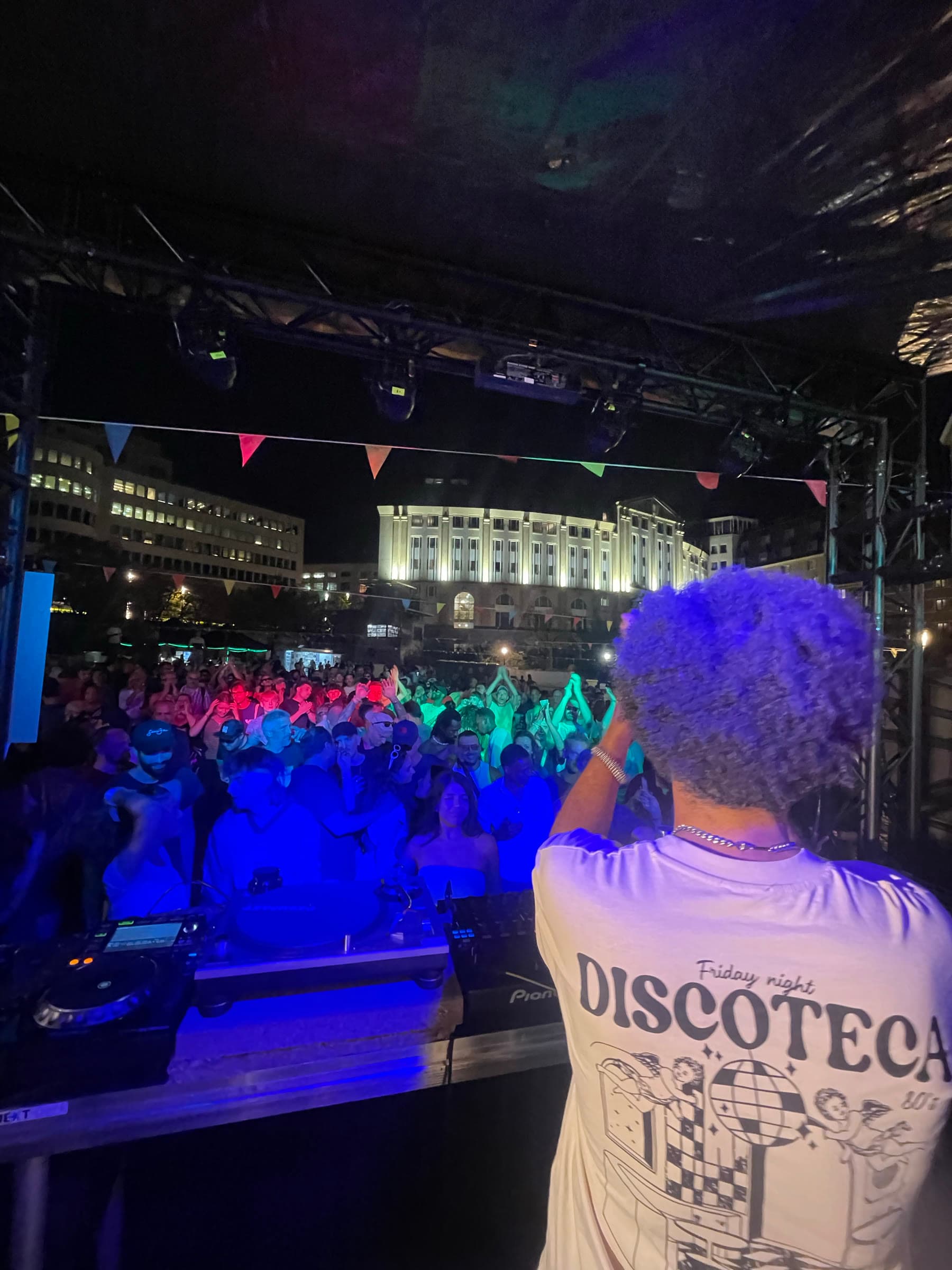 Hands up in the crowd under blue light at the front of the booth.